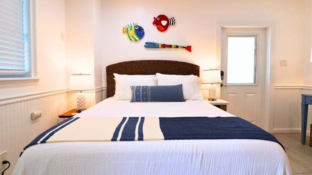 A neatly made bed with a striped bedspread, two bedside lamps, and decorative fish wall art.