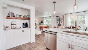 Una cocina moderna con armarios blancos, lavavajillas y un comedor con mesa y sillas blancas.