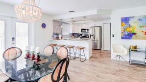 Una cocina moderna con gabinetes blancos, electrodomésticos de acero inoxidable y una isla central con taburetes de bar.