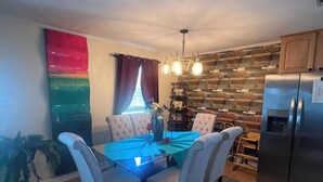 Un comedor con una mesa preparada para cuatro personas, un refrigerador y una pared de ladrillo.