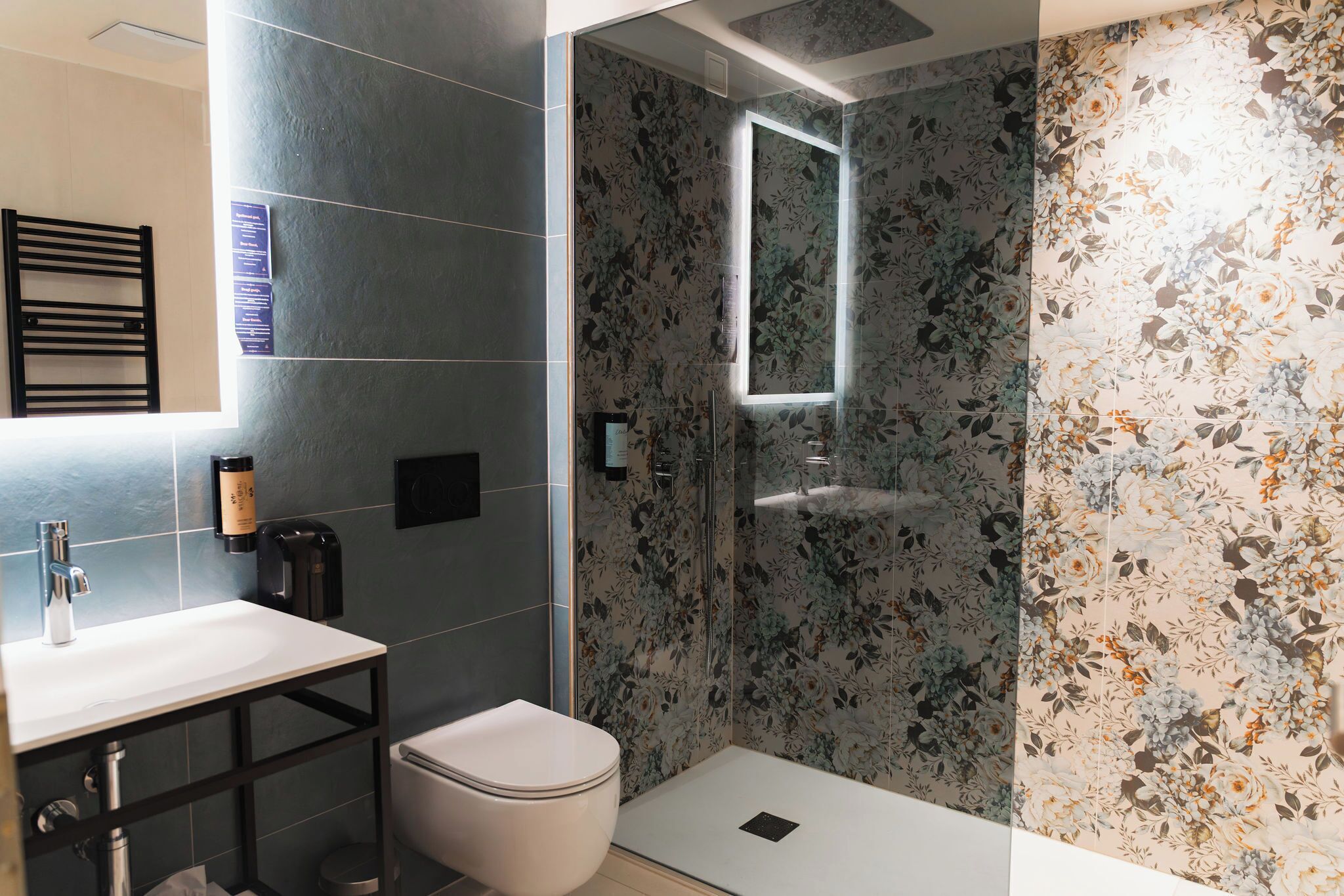 A modern bathroom with a white sink, a toilet, and a shower area with floral-patterned tiles.