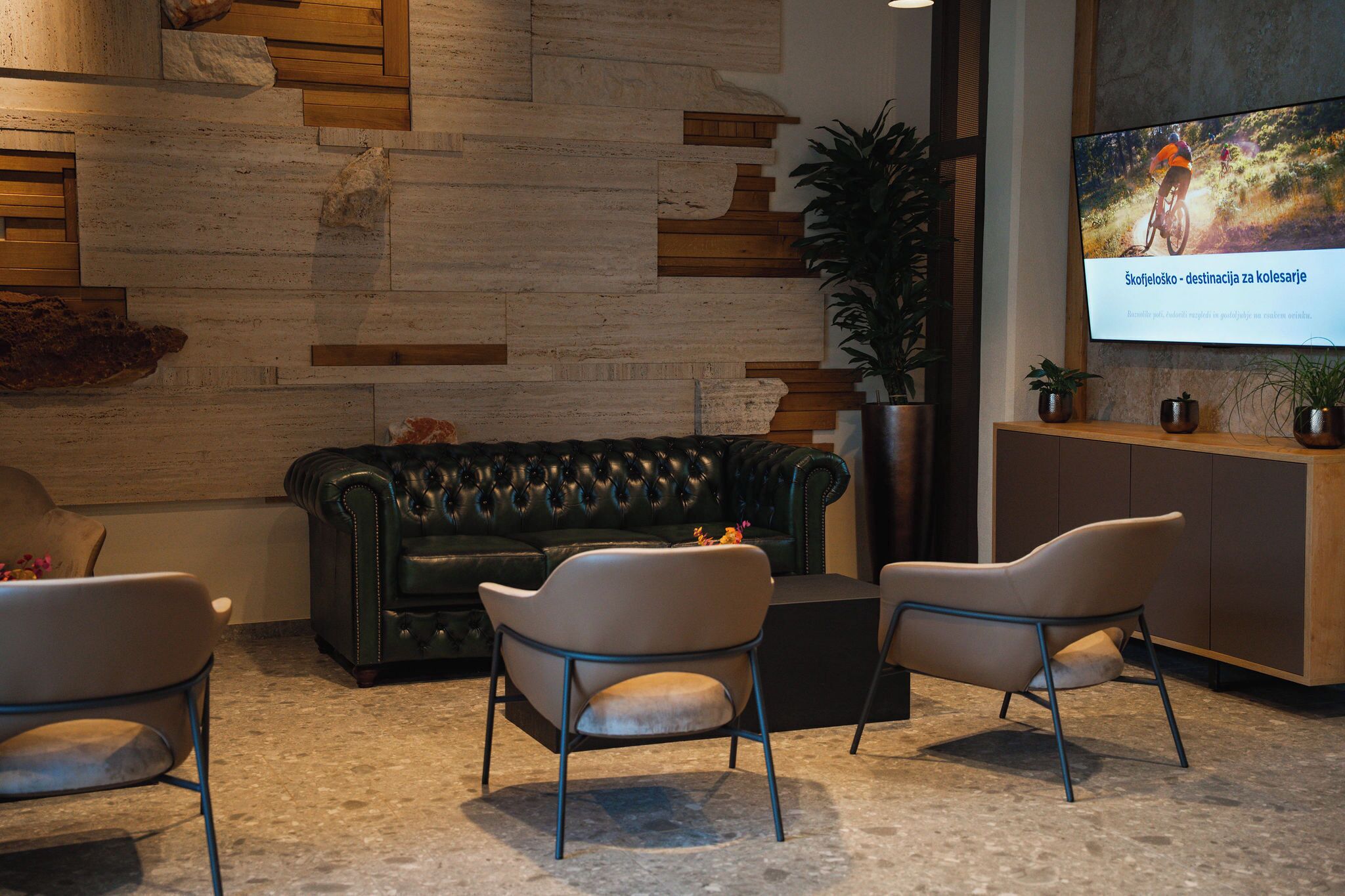 Een moderne zithoek met een leren bank, twee fauteuils en een salontafel. Een groot scherm toont een fietsevenement.