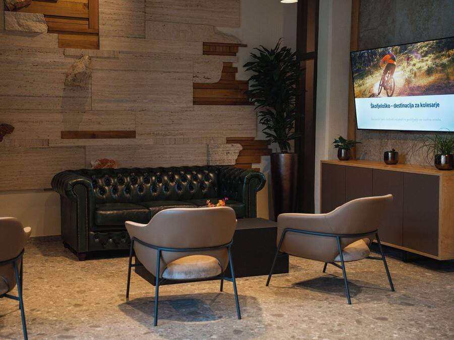 Een moderne zithoek met een leren bank, twee fauteuils en een salontafel. Een groot scherm toont een fietsevenement.