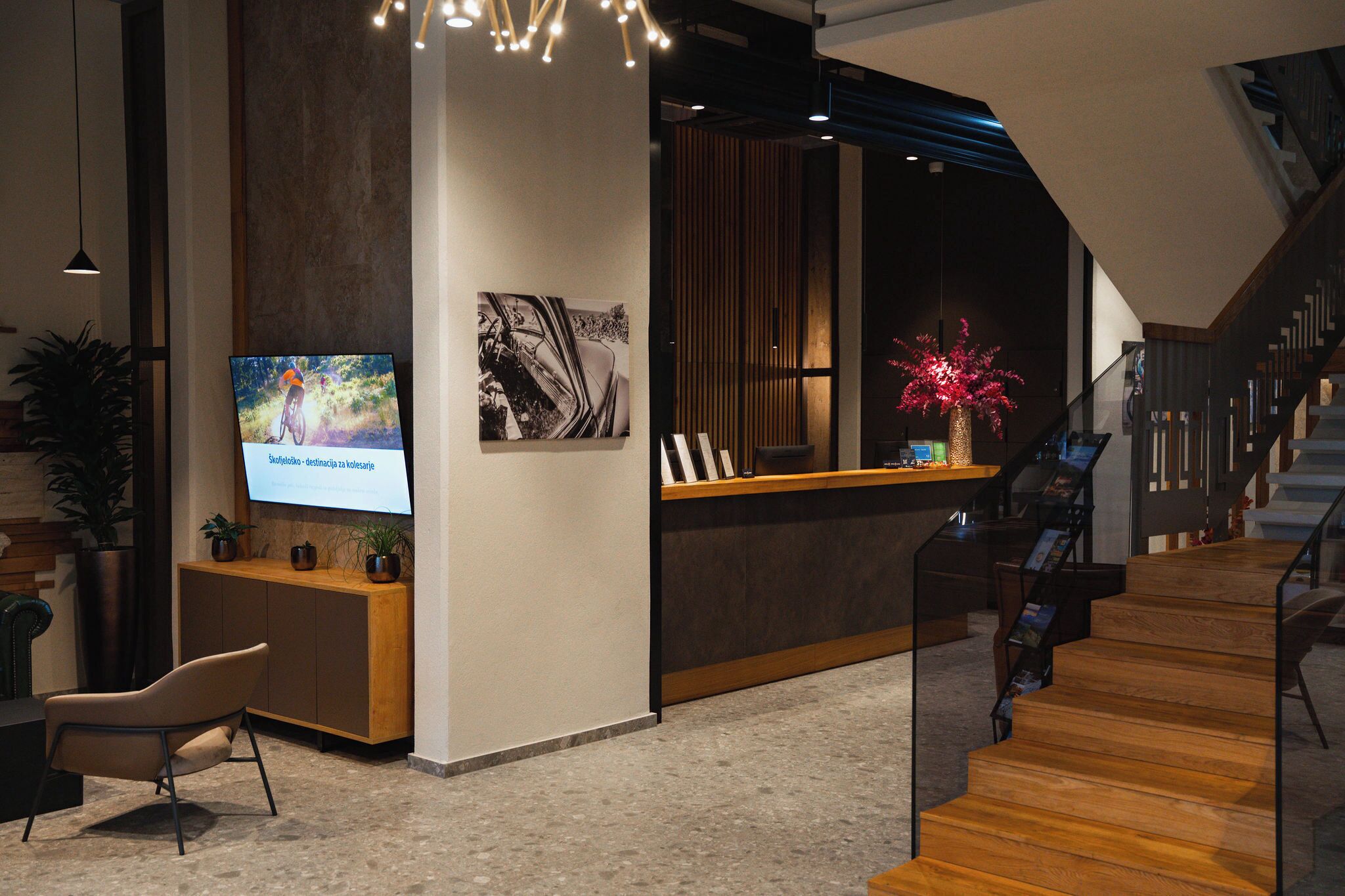 A modern reception area with a wooden reception desk, a mounted television, and a staircase leading to an upper floor.