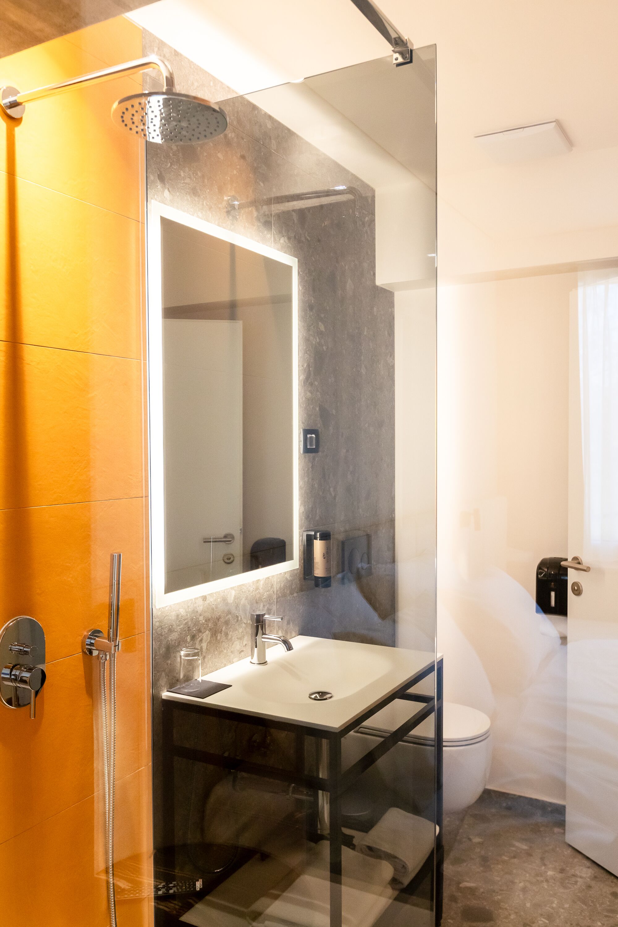 A modern bathroom with a glass shower enclosure, a large mirror, a white sink, and a toilet.