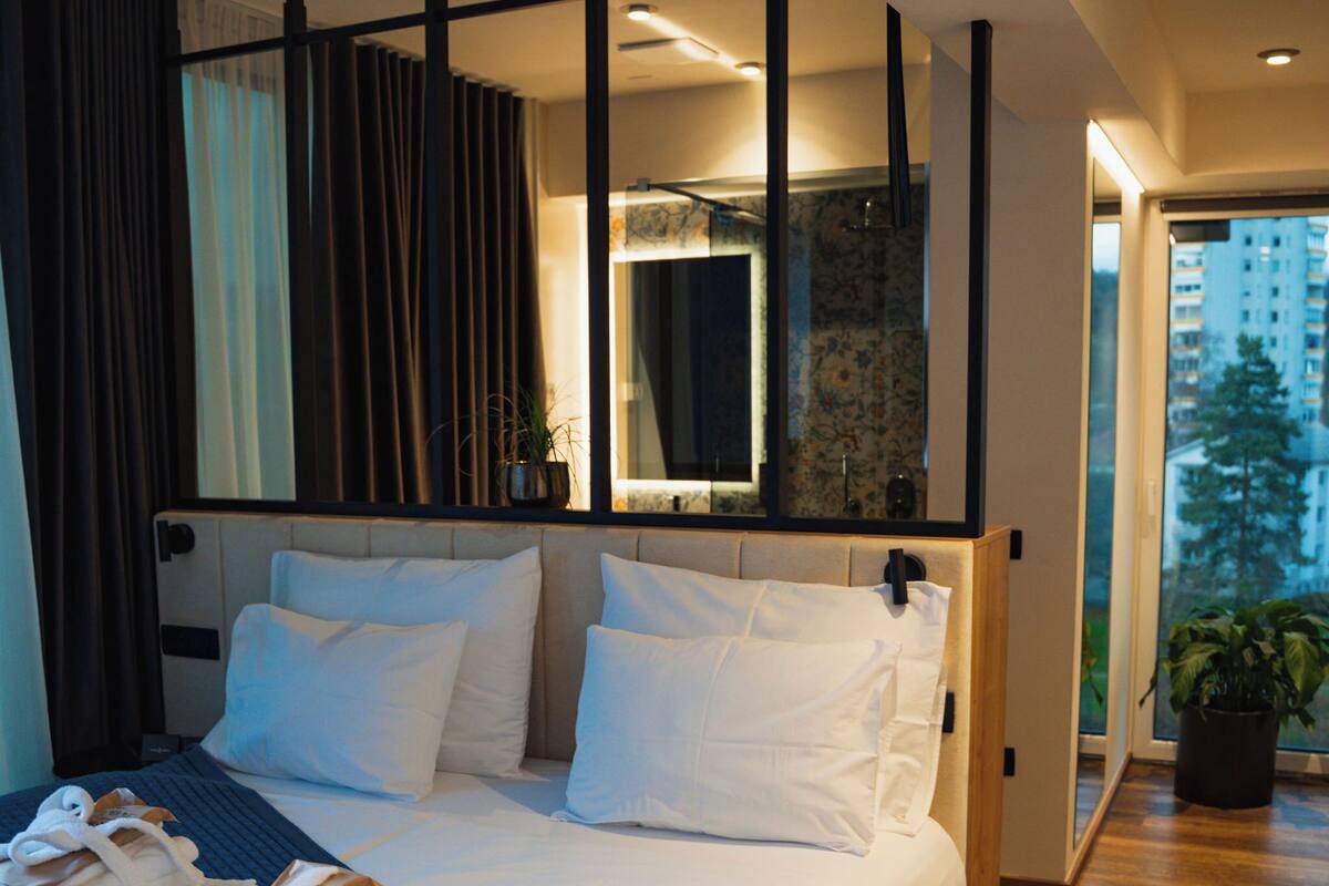 A modern hotel room with a large bed, a mirror, and a view of the city.