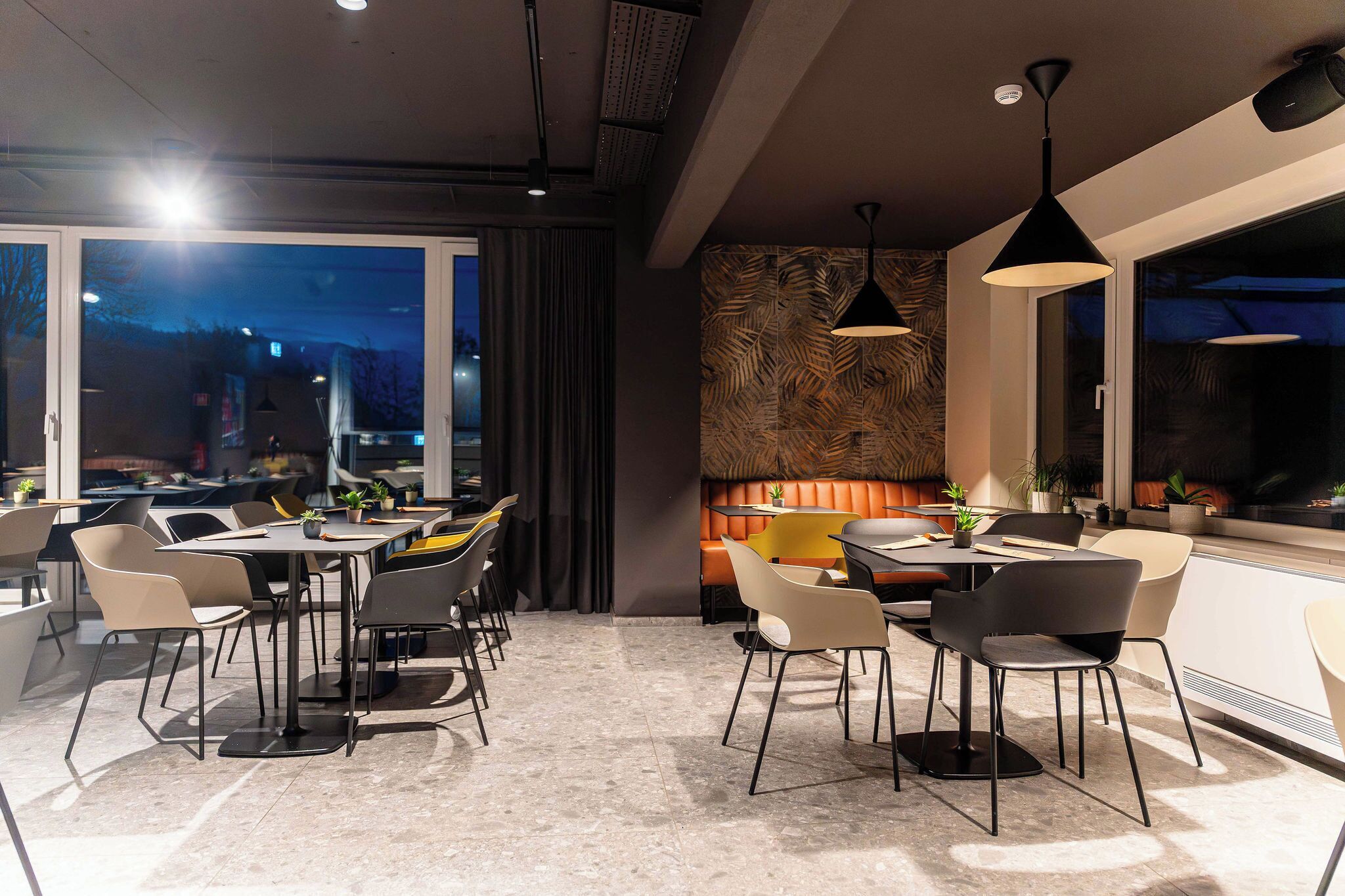 Un comedor moderno con mesas y sillas, ventanas amplias y un muro con diseño.