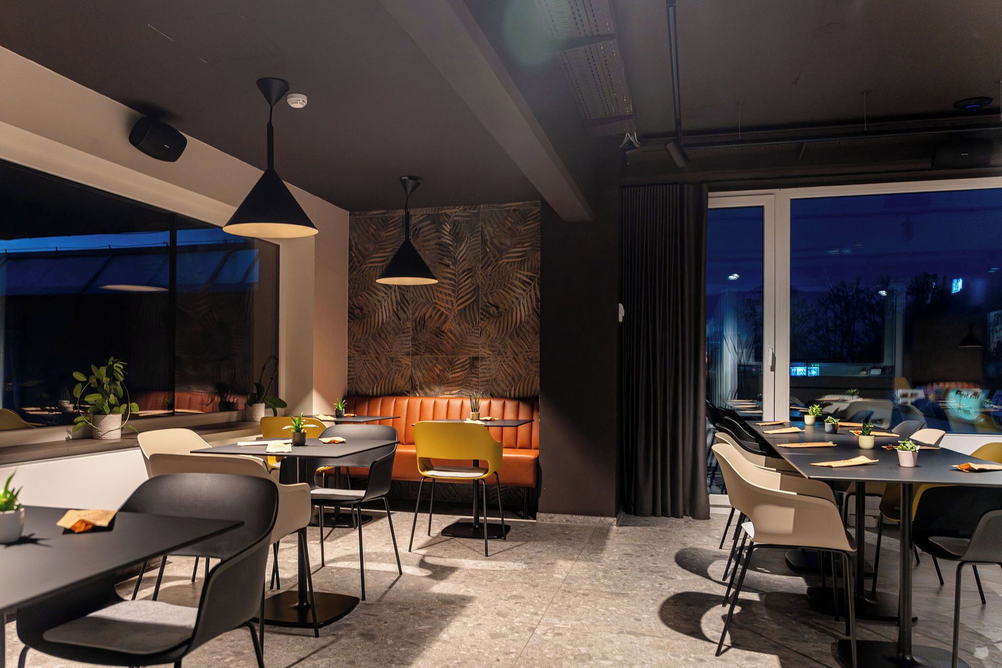 A modern dining area with a mix of black and yellow chairs, a central orange booth, and pendant lighting.