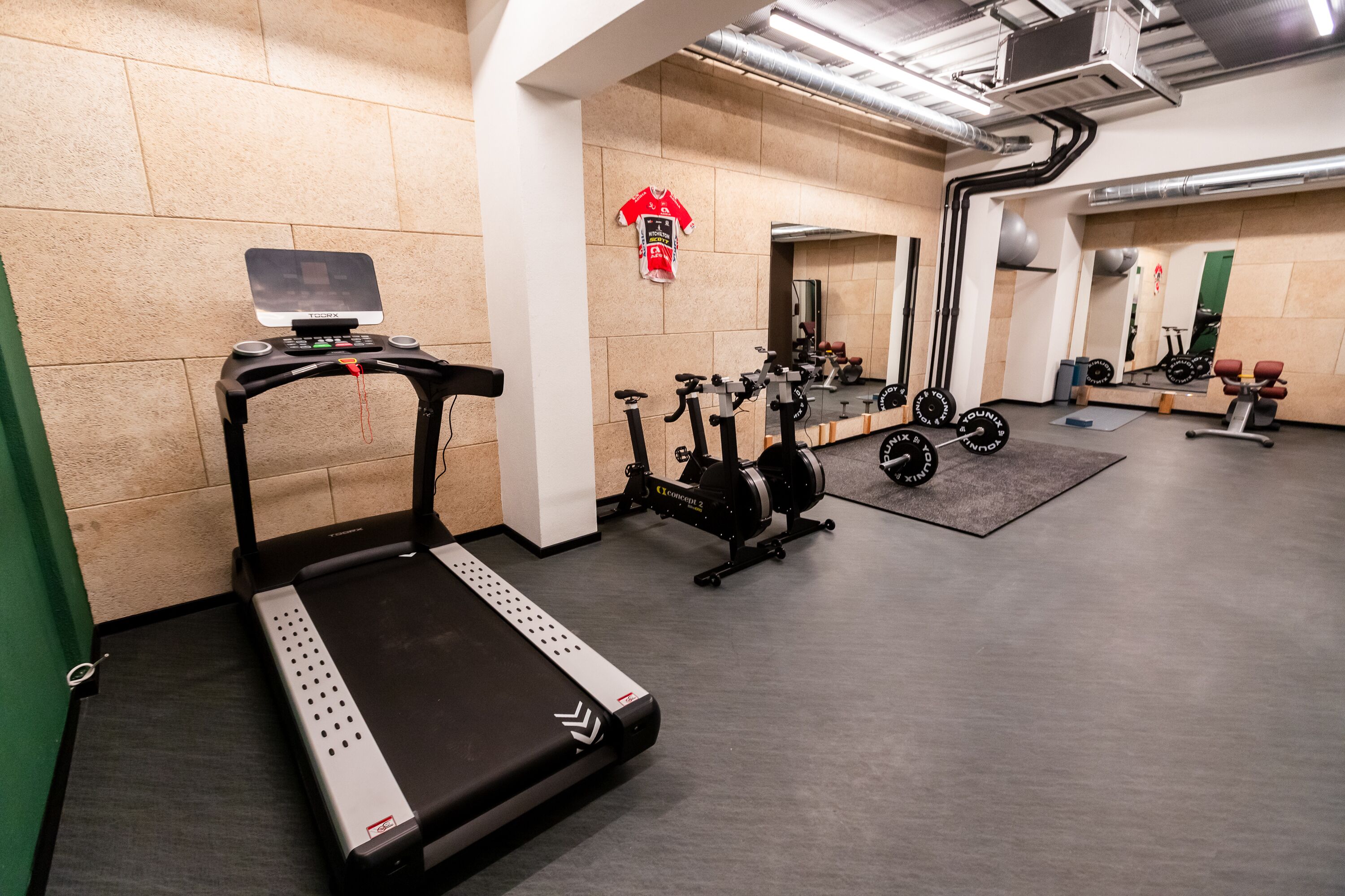 Een fitnessruimte met een loopband, hometrainers en gewichten.