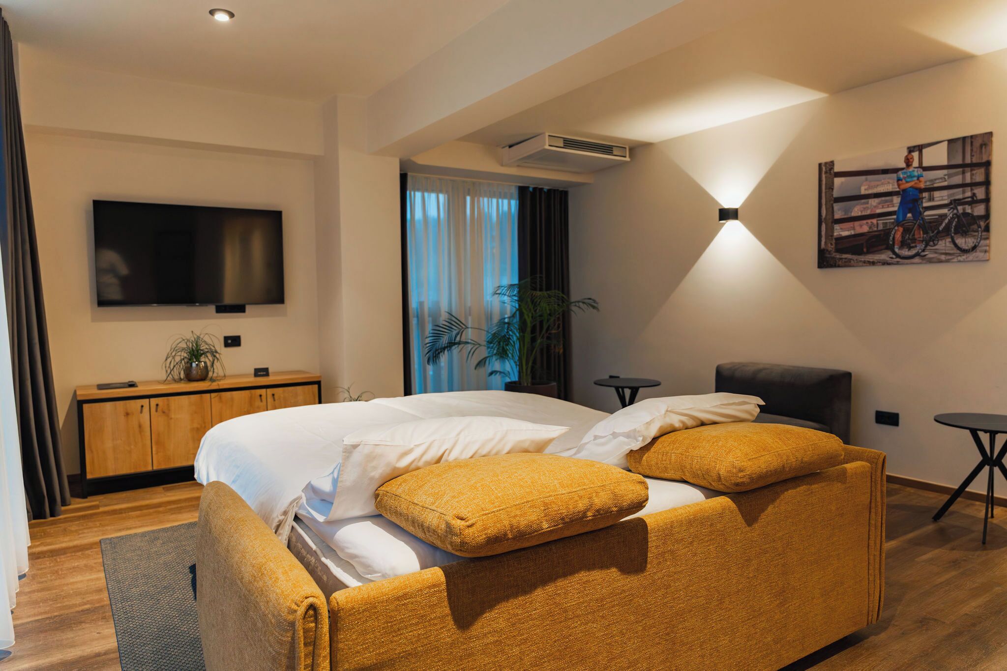 Une chambre d’hôtel moderne avec un grand lit, un téléviseur fixé au mur, une petite table et un tableau accroché au mur.