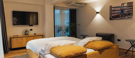 Une chambre d’hôtel moderne avec un grand lit, un téléviseur fixé au mur, une petite table et un tableau accroché au mur.