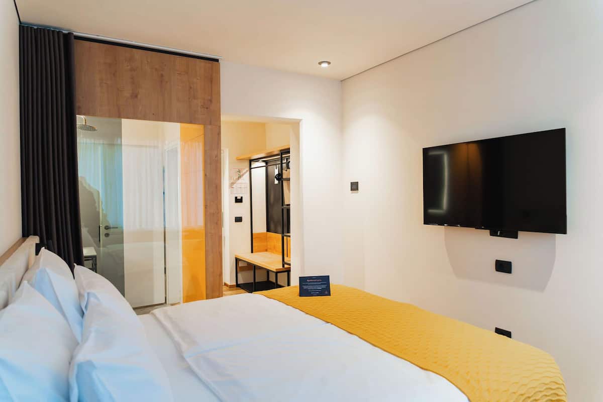 A hotel room with a bed, a television mounted on the wall, and a sliding door leading to a bathroom.