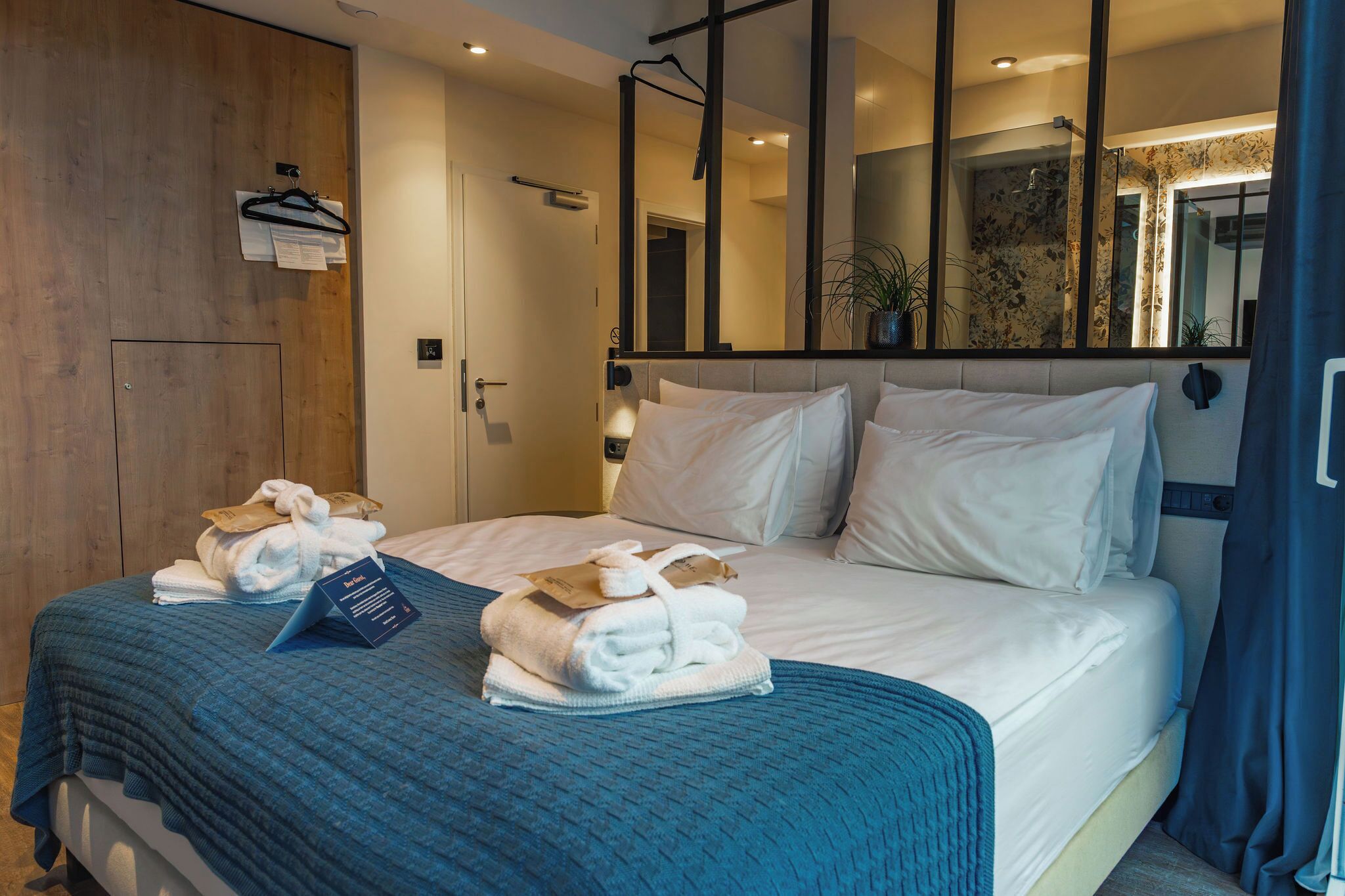 A hotel room with a large bed, a wooden wardrobe, a mirror, and a blue blanket.