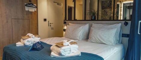 A hotel room with a large bed, a wooden wardrobe, a mirror, and a blue blanket.