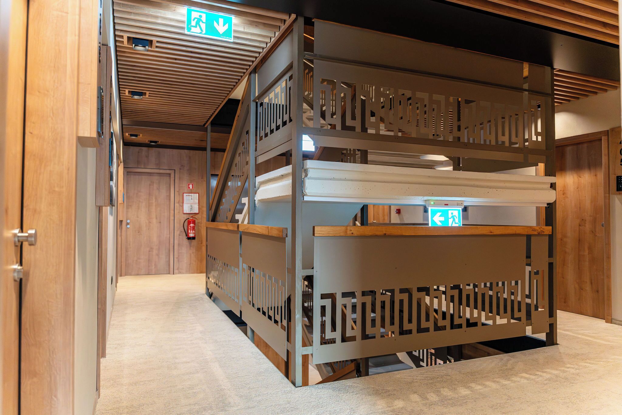 A hotel room with a wooden floor, a bed with a headboard, and a wooden partition with a geometric pattern.