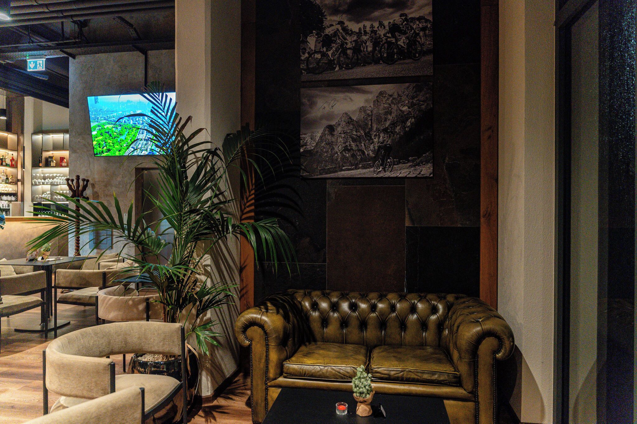 Een hal met een leren bank, fauteuils, een salontafel en een televisiescherm dat een landschap toont.