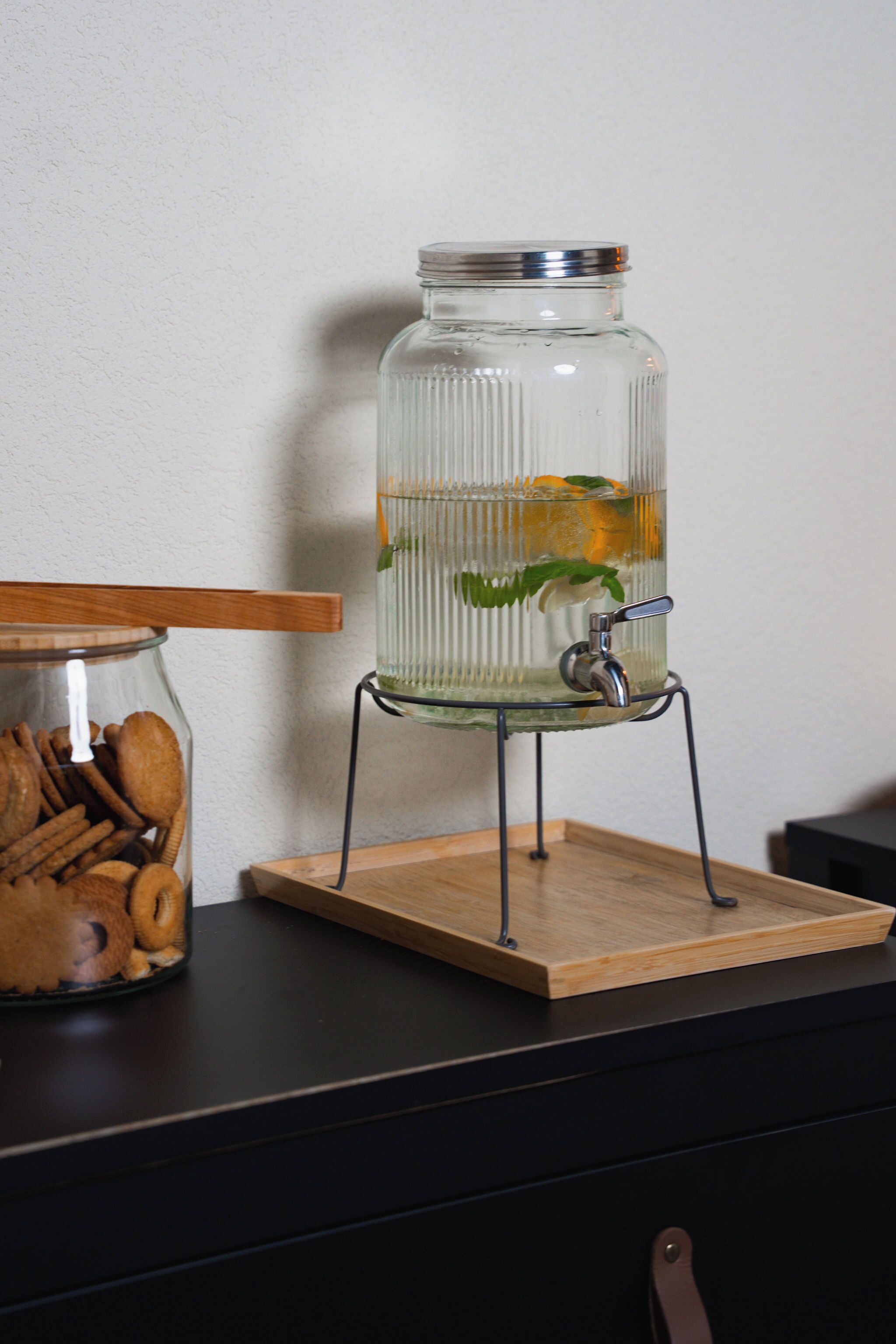 A glass jar with a metal lid on a wooden stand, containing cookies and a water dispenser with a metal spout.
