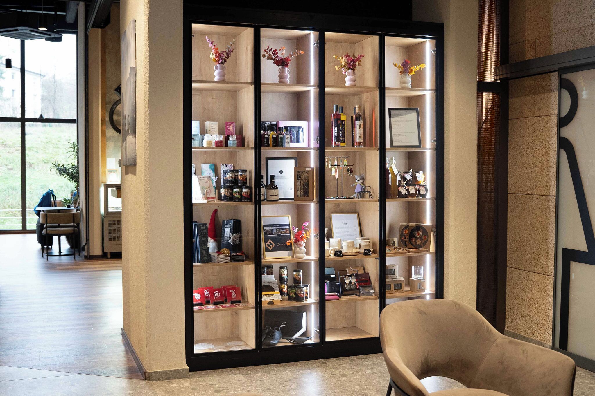 Zona de recepción con una vitrina de madera que contiene diversos objetos, un sillón color crema y un ventanal con vistas al exterior.