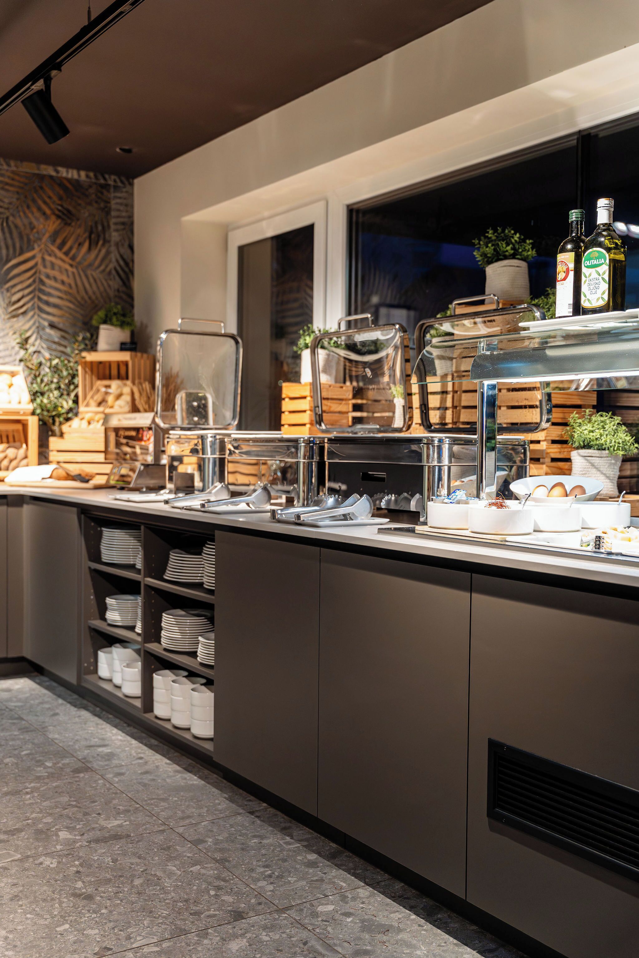 A modern kitchen with a buffet setup, including a coffee station, food containers, and a window with a view.