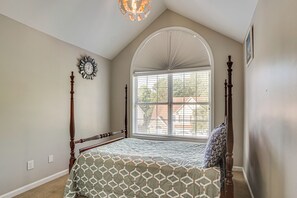 A bedroom with a bed, a clock, and a window with blinds.