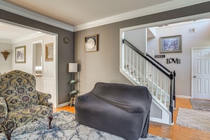 A living room with a patterned armchair, a dark sofa, a staircase, and a wall with a 'LOVE' sign.