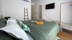 Une chambre à coucher avec un lit, des oreillers, un téléviseur à écran plat, un climatiseur, une échelle et un plancher en bois.