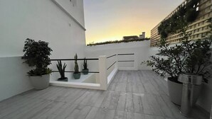 Une terrasse sur le toit, dotée d’une balustrade, de plantes en pot et offrant une vue sur les bâtiments en arrière-plan.