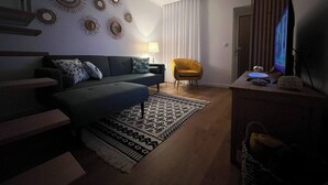 Un salon comprenant un canapé, un fauteuil jaune, un téléviseur et des miroirs décoratifs fixés au mur.
