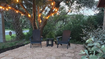 Une terrasse en pierre avec des carreaux hexagonaux, deux chaises en bois et un arbre décoré de guirlandes lumineuses.