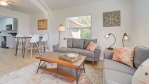 A modern living room with a grey sofa, a wooden coffee table, and a dining area with white chairs. - Surfside Beach House (St. Augustine)