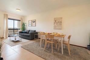 Un salon moderne avec un canapé gris, une table à manger avec des chaises et une grande fenêtre.