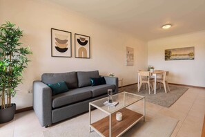A modern living room with a grey sofa, a glass coffee table, and a dining area with a wooden table and chairs.