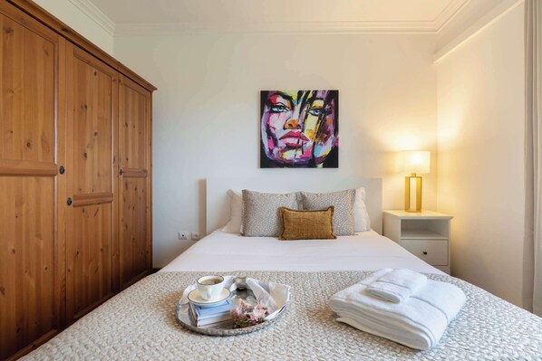 Une chambre d’hôtel avec une grande armoire en bois, un lit avec du linge de lit blanc, un tableau au mur et une table de chevet avec une lampe.