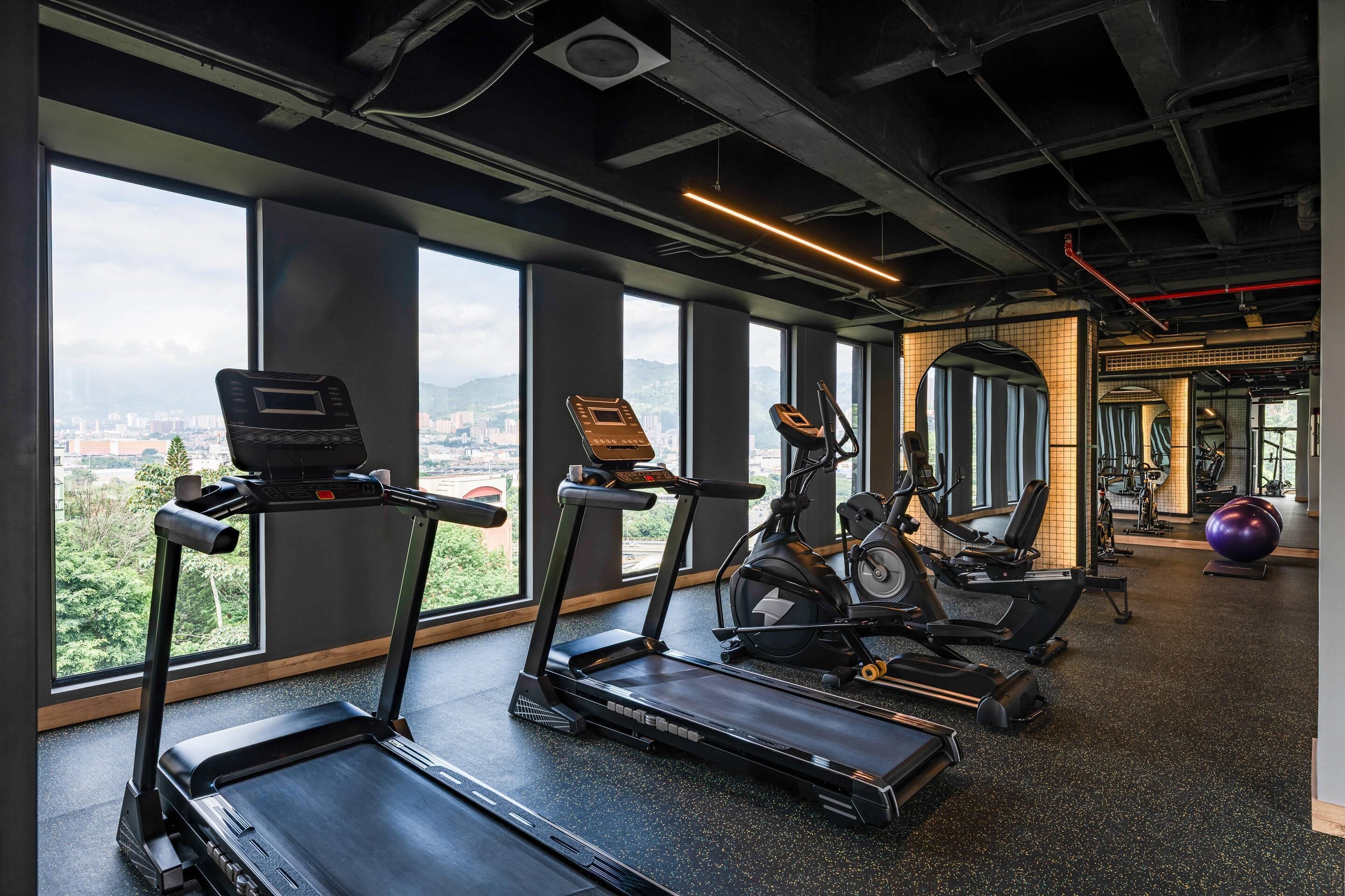Una palestra con tapis roulant, ellittiche e cyclette, ampie finestre vista città e palle per esercizi.