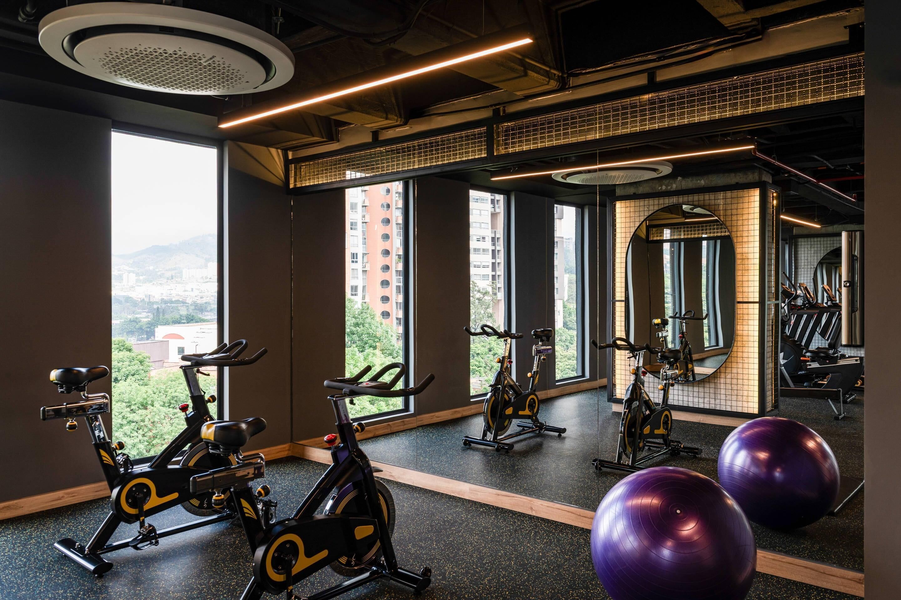 A gym with stationary bikes, exercise balls, and a large mirror.