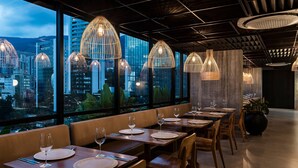 A restaurant with tables set for dining, large windows offering a city view, and hanging pendant lights. - Faranda Collection Medellin, a Member of Radisson Individuals (Medellín)