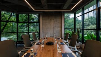 Un salón de conferencias con una larga mesa de madera, varias sillas y amplias ventanas que dan a zonas verdes.