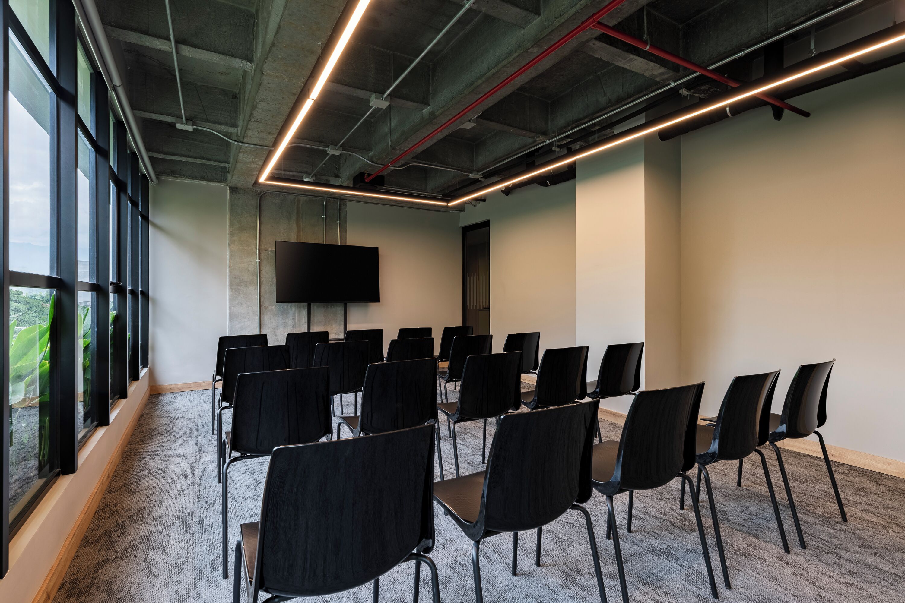 Un salón de conferencias con filas de sillas, un televisor de pantalla plana grande y suelo alfombrado.