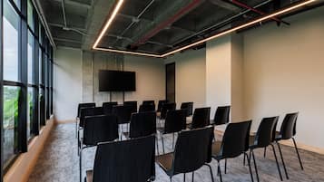 Un salón de conferencias con filas de sillas, un televisor de pantalla plana grande y suelo alfombrado.