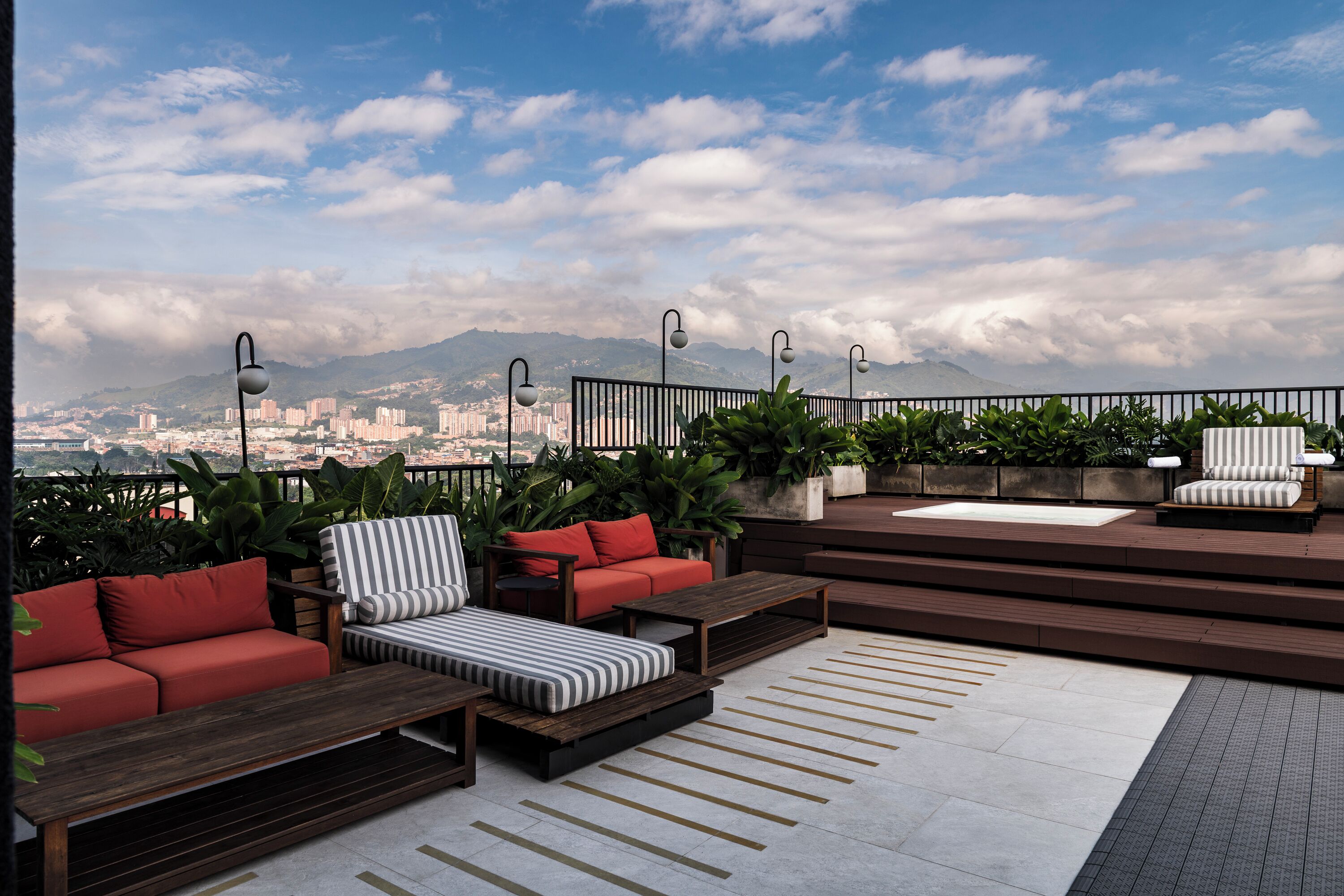 A rooftop terrace with outdoor seating, including sofas and chairs, surrounded by potted plants.