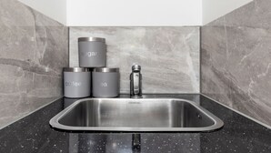 Eine Küche mit Spüle aus Edelstahl, einem modernen Wasserhahn und drei Behältern mit den Aufschriften Zucker, Kaffee und Tee.