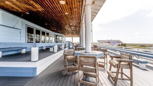 Una terraza de madera con bancos y mesas, con vistas a la costa.