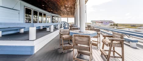 Una terraza de madera con bancos y mesas, con vistas a la costa.