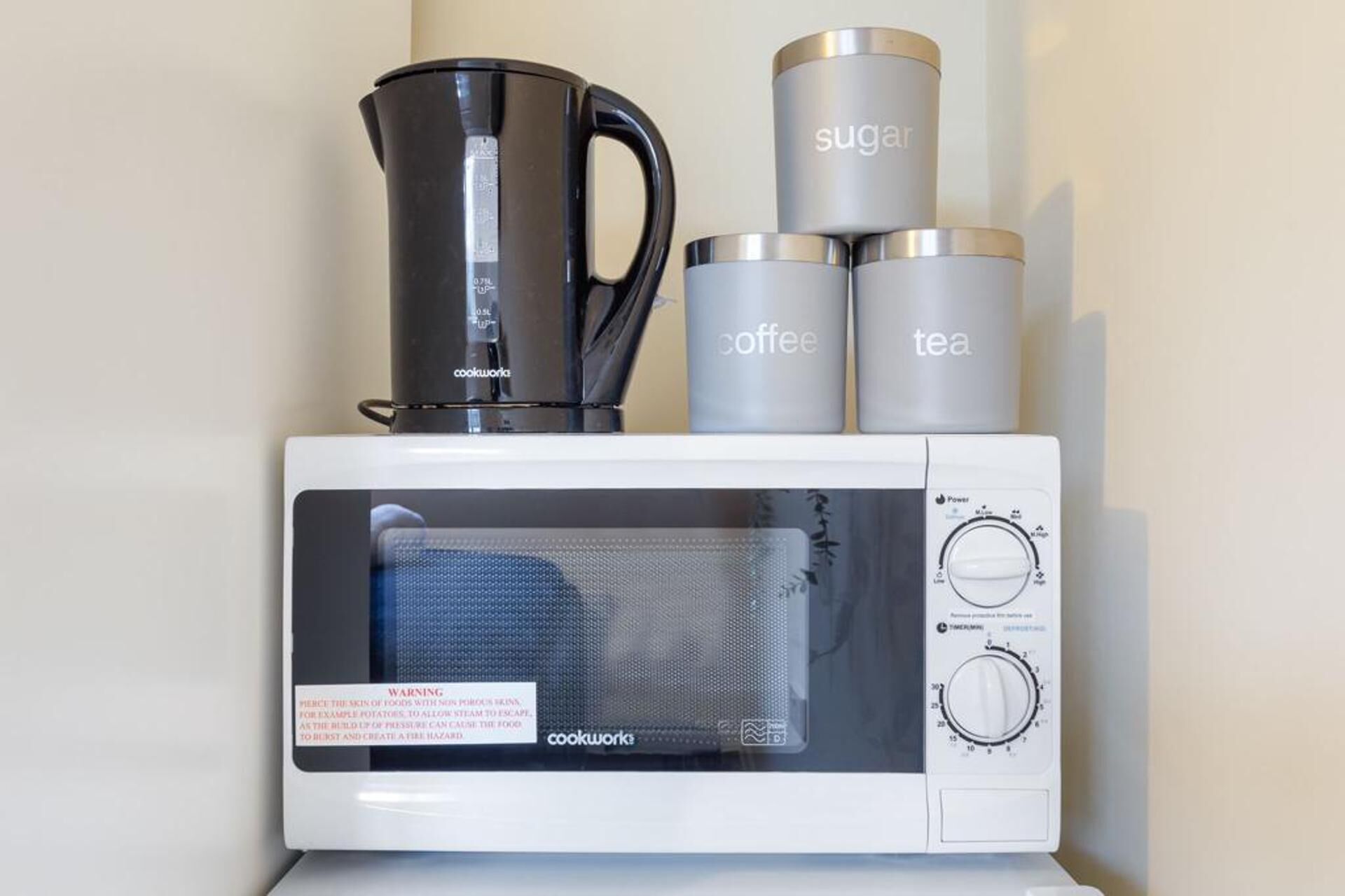 A white microwave with a coffee pot, a sugar container, and a tea container on top.