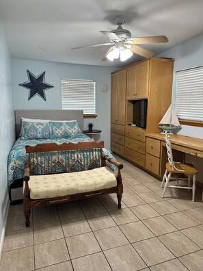 A bedroom with a bed, a wooden desk, a chair, a ceiling fan, and a star decoration on the wall.