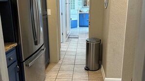 A kitchen with a stainless steel refrigerator, a trash can, and a door leading to a bathroom. - Surfside Shangri-La (Daytona Beach)