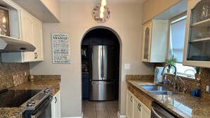 A modern kitchen with granite countertops, stainless steel appliances, and a central island. - Surfside Shangri-La (Daytona Beach)