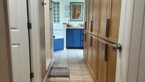 A hallway with a tiled floor leading to a bathroom with a sink and mirror. There are wooden cabinets and a door on the right side. - Surfside Shangri-La (Daytona Beach)