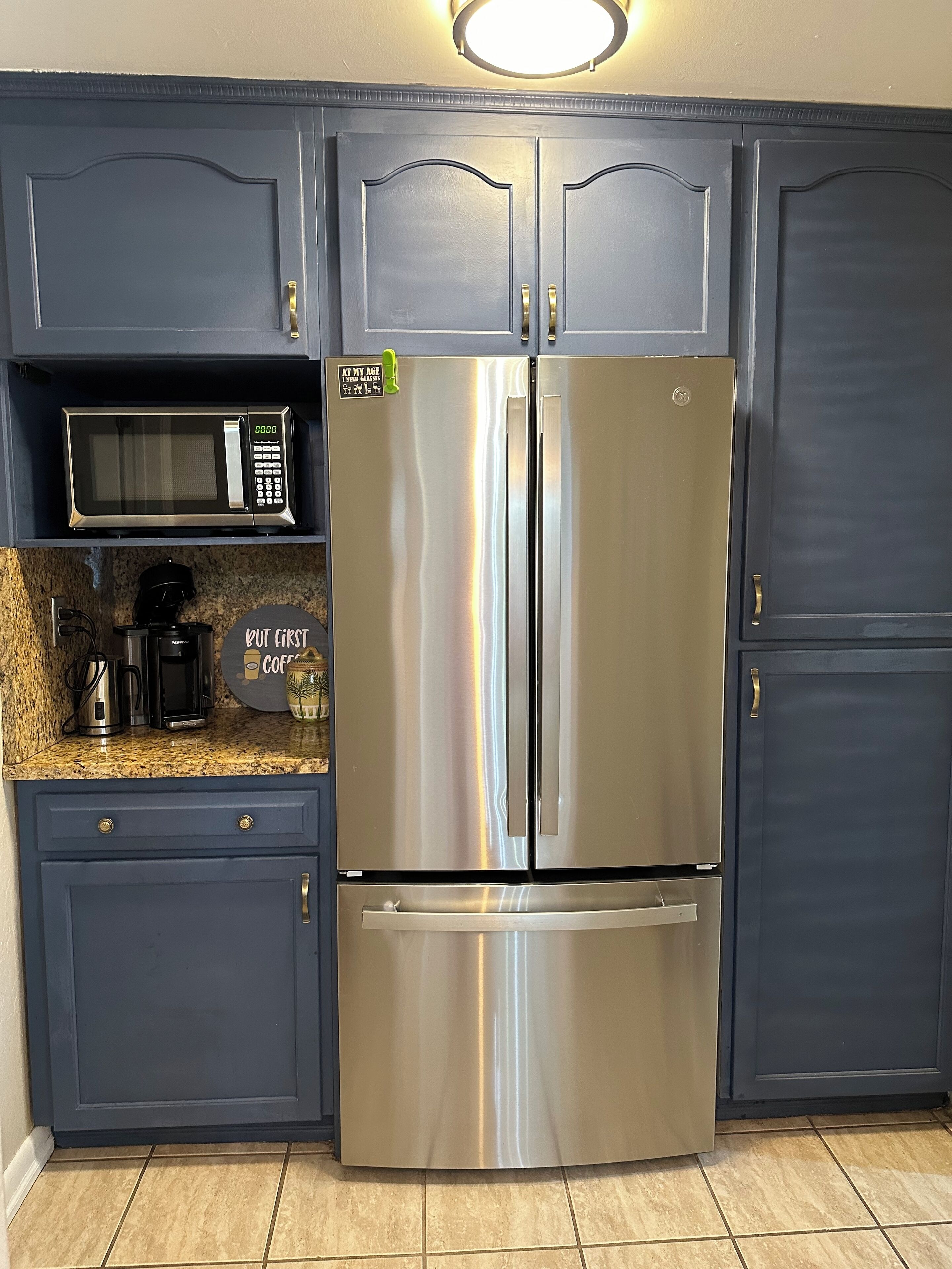 A kitchen with dark blue cabinets, a stainless steel refrigerator, a microwave, and a coffee maker on the countertop.
