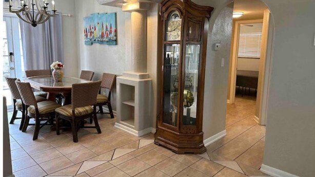 A dining area with a round table, chairs, a chandelier, a painting, and a wooden cabinet. - Surfside Shangri-La (Daytona Beach)